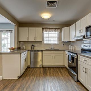 A modern kitchen featuring white cabinets, stainless steel appliances, and hardwood flooring.