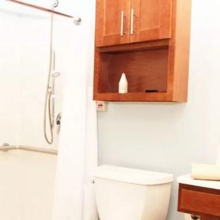 A clean and modern bathroom featuring a shower with a white curtain, a toilet, and a wooden wall cabinet.