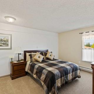 A cozy bedroom featuring a neatly made bed with checkered bedding and matching nightstands, illuminated by natural light streaming through the window.