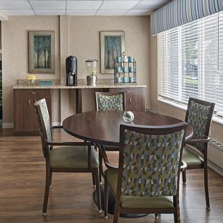 A cozy dining area with a wooden table and chairs, complemented by a coffee station and decorative paintings.