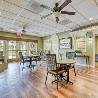 A cozy dining area with tables and chairs, featuring ceiling fans and large windows for natural light.