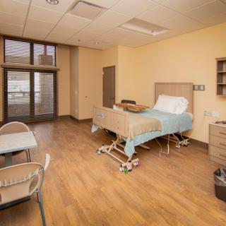 A clean and spacious hospital room with a single bed and chairs.