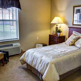 A cozy bedroom with a single bed, nightstand, and lamp by the window.