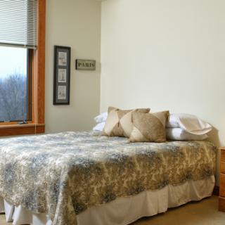 A cozy bedroom featuring a neatly made bed and natural light coming through the window.