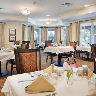 A well-decorated dining room with neatly arranged tables covered with white tablecloths and set with glasses and napkins.