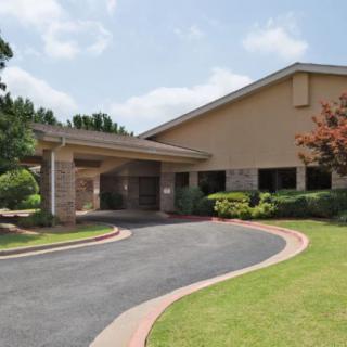 A building with a covered entrance and a curved driveway surrounded by landscaping.