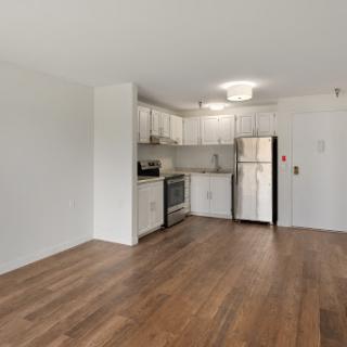 A modern kitchen area featuring white cabinetry and wood flooring, perfect for a cozy apartment.