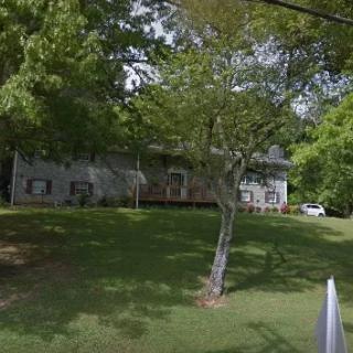 A suburban house surrounded by trees and a well-maintained lawn.