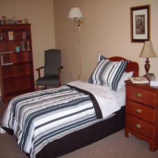A cozy bedroom with a single bed featuring striped bedding, accompanied by a nightstand and a bookshelf.