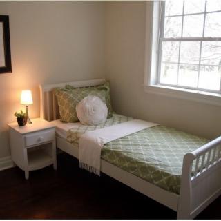 A cozy bedroom with a single bed, nightstand, and lamp by the window.