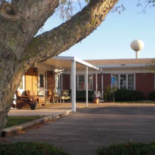 A cozy residential building surrounded by trees, featuring a well-maintained parking area under a clear blue sky.