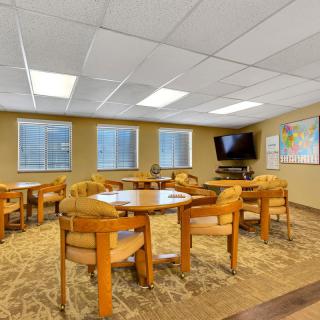 A well-lit meeting room with multiple tables and chairs, featuring a wall-mounted television and world maps.