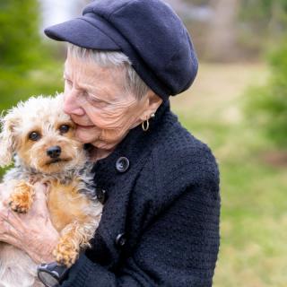An elderly woman lovingly holding her small dog outdoors.