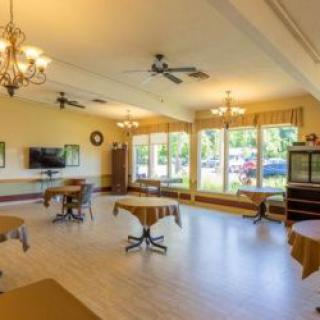 A bright and spacious room with tables and chairs arranged, large windows letting in natural light, and decorative chandeliers hanging from the ceiling.