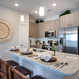 A modern kitchen with a sleek design featuring stainless steel appliances, a marble countertop with bar seating, and decorative elements.