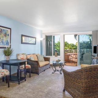A cozy living room with wicker furniture and a balcony opening to lush greenery.