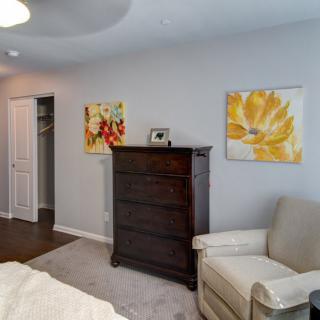 A cozy bedroom corner with a dark wooden chest of drawers, a comfortable chair, and colorful artwork on the walls.