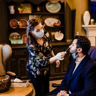A healthcare worker administers a COVID-19 test indoors, both wearing masks for safety.