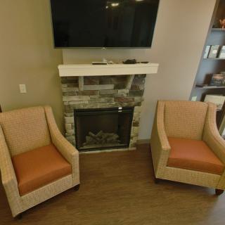 A cozy living room setup with two chairs facing a fireplace and a TV mounted above.