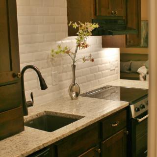A modern kitchen with a sleek countertop, featuring a sink, stove, and elegant backsplash.