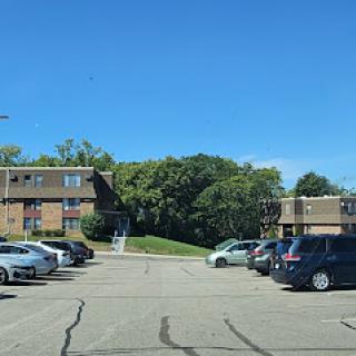 A serene view of a parking lot surrounded by apartment buildings and greenery under a clear blue sky.