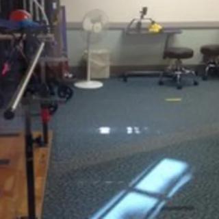 An office space with chairs, equipment, and a fan, illuminated by window light.