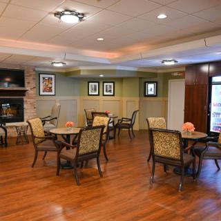 A cozy dining area with wooden floors, tables and chairs, a fireplace, and decorative lighting.