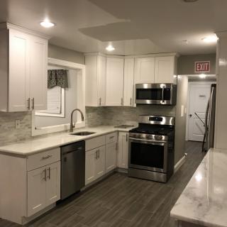 A modern kitchen with white cabinets and stainless steel appliances, featuring a marble countertop and recessed lighting.