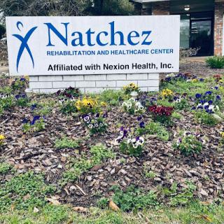 Sign for Natchez Rehabilitation and Health Care Center, surrounded by colorful flowers.