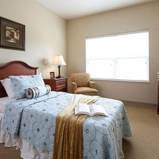 A cozy bedroom with a single bed, bedside lamp, and armchair by the window.