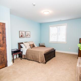 A cozy bedroom featuring a neatly made bed, soft carpet, and calming blue walls.