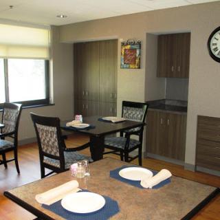 A cozy dining area featuring tables and chairs, illuminated by natural light, complete with a kitchenette and decorative elements.