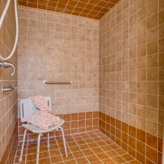 An accessible walk-in shower with tiled walls and a shower chair.