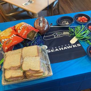 A Seattle Seahawks-themed table setup with sandwiches, chips, and snacks.