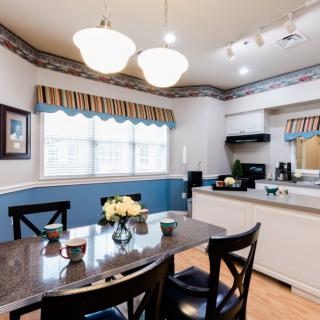 A cozy kitchen and dining area with a table set for four, bright lighting, and large windows with curtains.