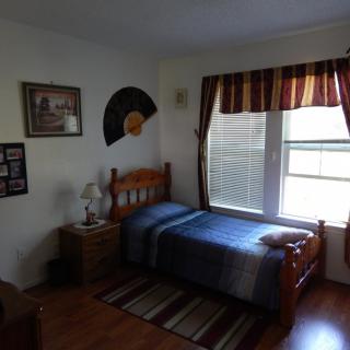 A cozy bedroom with a single bed, window with striped curtains, and decorated with wall art.