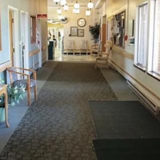 A well-lit corridor with chairs and carpeted flooring, leading to a reception area.