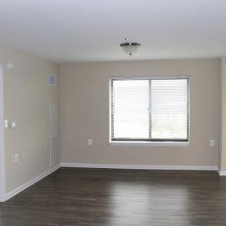 An empty room with neutral-colored walls and dark hardwood flooring, featuring a large window.