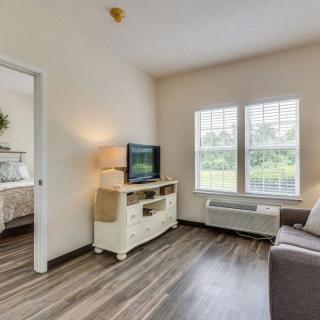 A cozy living room with a sofa, television, and large windows, featuring wooden flooring.