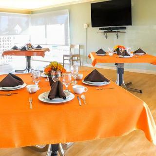 A brightly lit dining room featuring tables with orange tablecloths, elegantly set with napkins and place settings.
