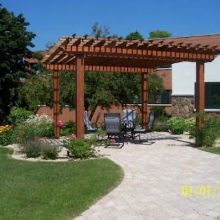 A backyard garden featuring a wooden pergola with outdoor seating and lush landscaping.