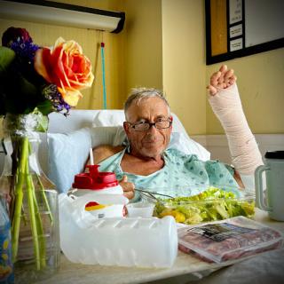 A patient in a hospital bed, enjoying a meal with flowers by their side.