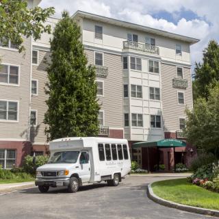 A shuttle bus parked in front of a multi-story residential building surrounded by trees.