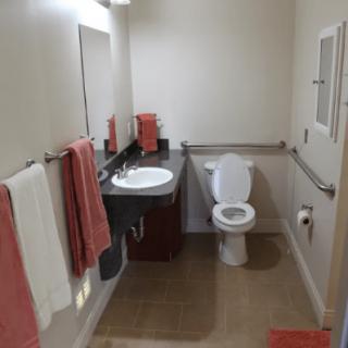A clean bathroom with a sink, toilet, and coral-colored towels.