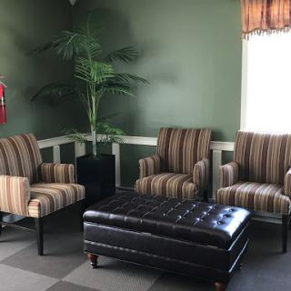 A cozy seating area featuring striped chairs and a dark ottoman, complemented by a potted plant against green walls.