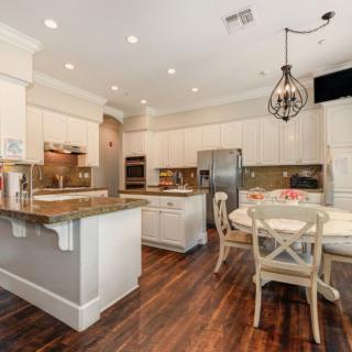A modern kitchen with white cabinets and a dining area, featuring hardwood floors and elegant chandelier lighting.