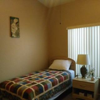 A small bedroom with a single bed, nightstand, and a window letting in natural light.