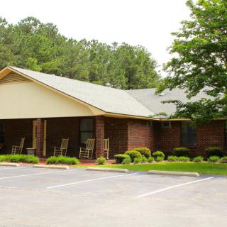 A small building with a parking lot in front, surrounded by trees and bushes.