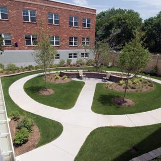 A landscaped courtyard with curved pathways and greenery adjacent to a brick building.
