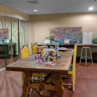 A cozy dining room with a wooden table, yellow chairs, and decorative elements including artwork and plants.